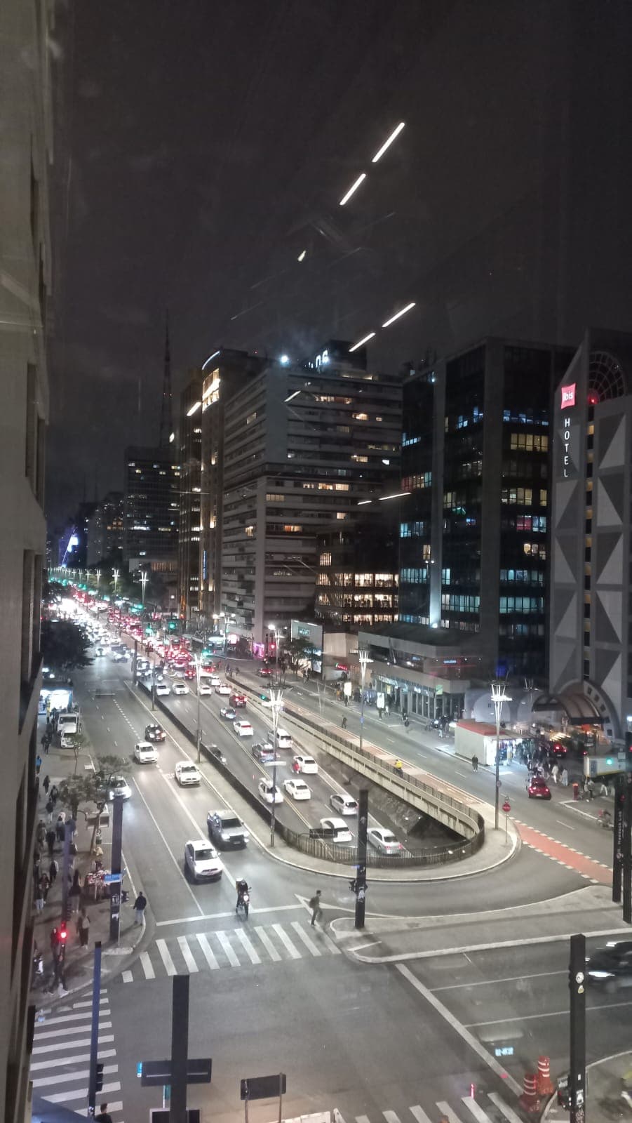 Vista noturna de uma avenida movimentada em São Paulo, com prédios e carros.