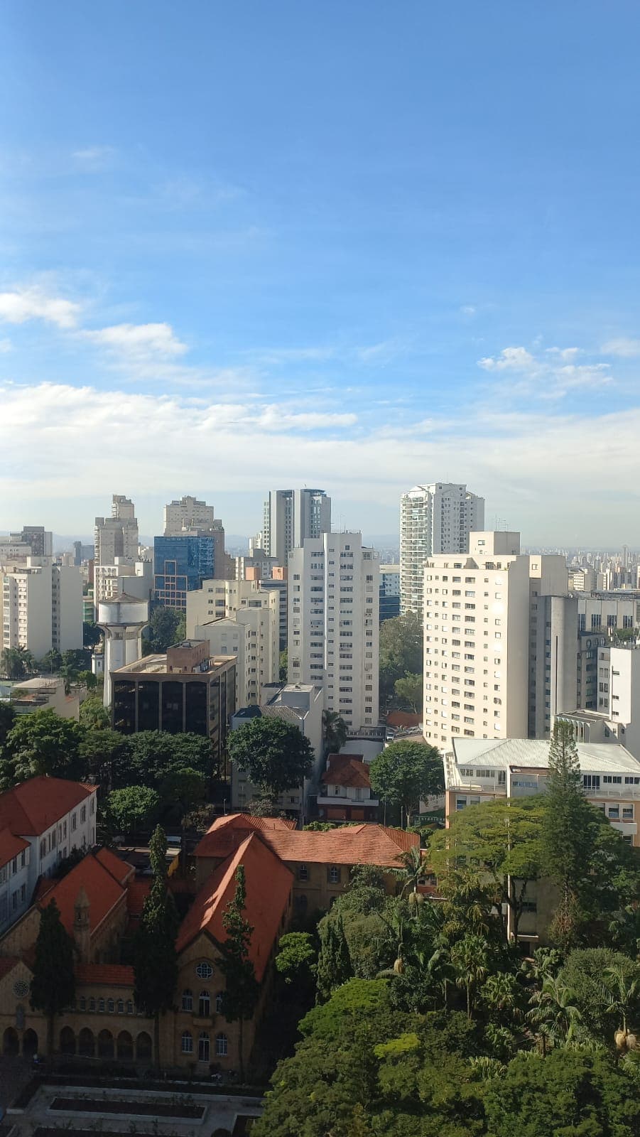 Vista urbana com prédios, céu azul e áreas verdes, sugerindo cidade, mudança e pertencimento.